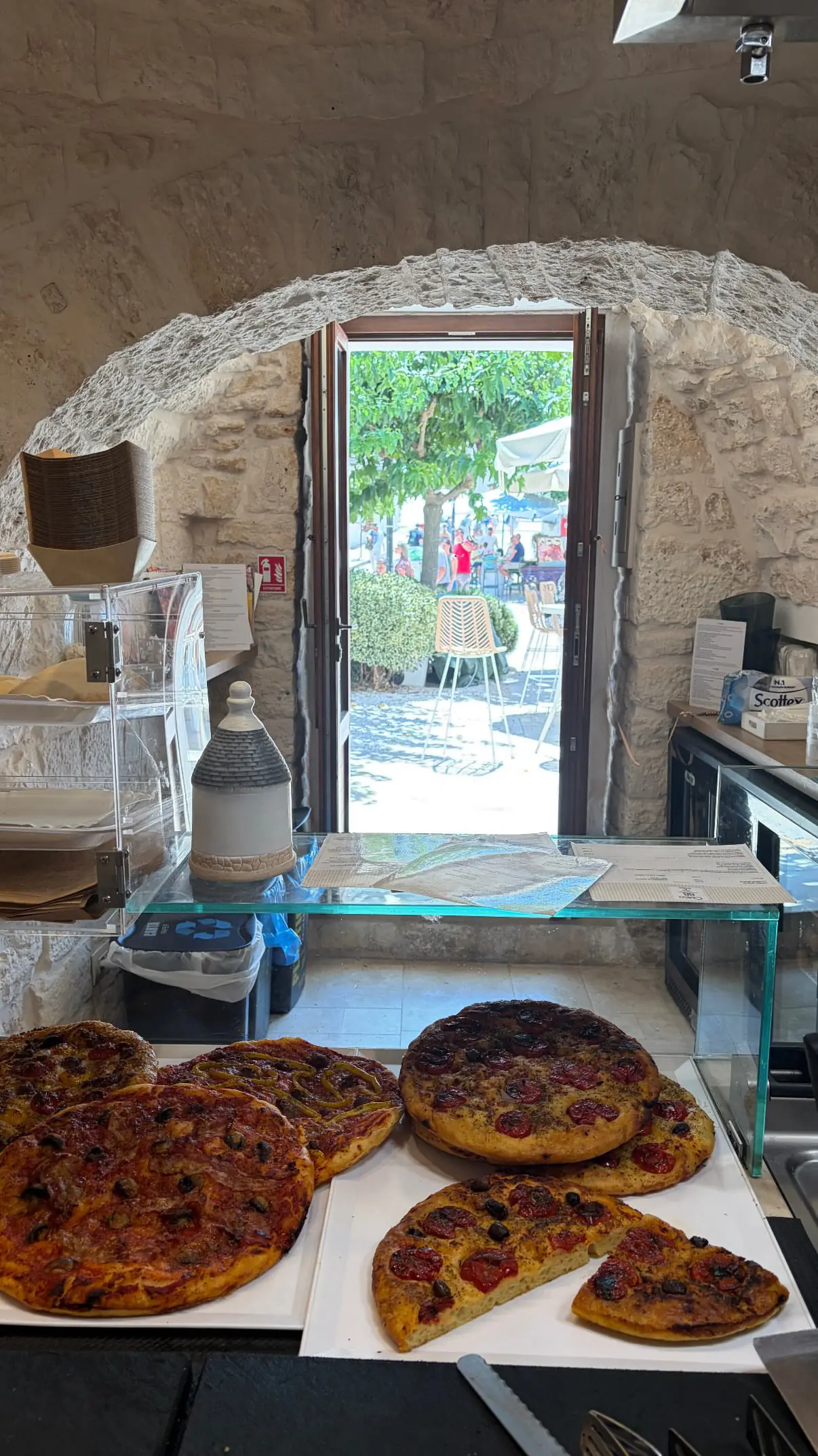 L'interno del trullo di Civico 88: l'arco di pietra sopra il banco e la porta aperta sui tavoli all'ombra